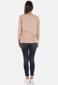 Maglione a maglia beige chiaro con scollo rotondo e maniche lunghe, abbinato a jeans skinny scuri e sneakers bianche, vista da dietro.