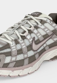 Αθλητικό παπούτσι Nike σε μπεζ και γκρι χρώμα με άνω μέρος από διάτρητο ύφασμα, λεπτομερές σύστημα κορδονιών και υφασμένη σόλα.