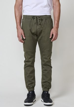 Pantalones jogger en verde oliva, hechos de un tejido suave, con una cinturilla elástica con cordón, piernas ajustadas y puños elásticos.