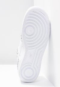 Baskets blanches avec une semelle en caoutchouc texturé présentant des motifs circulaires. Sur le côté, de petites rivets métalliques sont visibles ; le dessus a un design lisse.