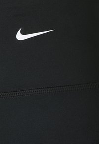 Black athletic leggings made of smooth fabric with a visible white Nike logo and subtle stitching detail along the waistband.