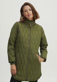 Olīvu zaļš quilted pūkains džemperis ar augstu apkakli, priekšējo rāvējslēdzēju un sānu kabatām. Iespējas ar ribotām aprocēm un vaļīgu piegriezumu.