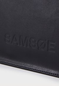 Sac en cuir noir avec logo "SAMSE" en relief, texture lisse et surpiqûres le long des bords. Forme rectangulaire compacte.