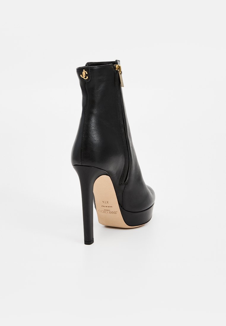 Bottines noires en cuir à talons hauts avec une texture lisse, détail de fermeture éclair dorée et avant à plateforme. Le talon aiguille ajoute de la hauteur.