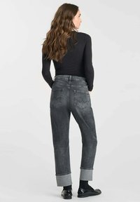 Jean en denim gris taille haute avec des ourlets retroussés, deux poches arrière et une texture subtile. Associé à un haut noir ajusté à manches longues et des chaussures.