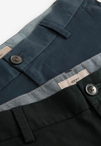 Twee broeken in marineblauw en donkergroen, met een stijlvolle rechte voorkant, knoopsluitingen en een gepatternde binnenvoering met een merkembleem.
