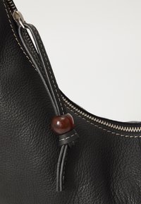 Borsa in pelle nera con superficie texturizzata, zip argentata e un accento in perla marrone su un cordino nero. Cuciture a contrasto visibili vicino alla zip.