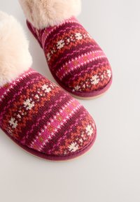 Chaussons en laine tricotée dans des tons de rose et bordeaux avec un revers en fausse fourrure. Présentent un motif combinant des éléments floraux et des rayures.