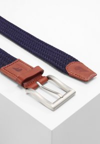 Geweven marineblauwe riem met een bruine leren uiteinde en een zilveren metalen gesp. Het materiaal is textuur en elastisch met een subtiel patroon.