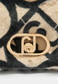 Sac tan avec un motif abstrait noir, comportant une fermeture dorée avec un détail de logo. Le matériau texturé donne une apparence douce, semblable à de la fourrure.
