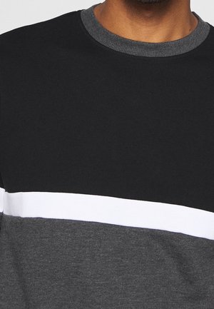 Mann trägt ein Color-Block-Sweatshirt mit schwarzen, weißen und dunkelgrauen horizontalen Streifen und einem gerippten Rundhalsausschnitt.