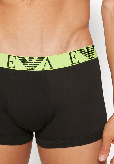 Boxer briefs de algodón negro con una cinturilla elástica verde neón que presenta un logotipo impreso en negro. Textura suave y diseño ajustado.