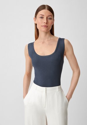 Dopasowany granatowy top na ramiączkach z szerokimi szelkami, w połączeniu z białymi spodniami o wysokim stanie. Gładka tekstura, minimalistyczny design.