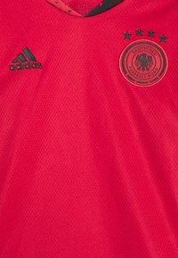 Maglia da calcio rossa realizzata in tessuto testurizzato, con logo Adidas nero, emblema della federazione calcistica tedesca e quattro stelle ricamate.