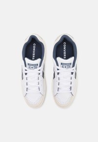 Bijele platnene tenisice s mornarsko plavim detaljima, s perforiranim prstom, bijelim vezicama i "CONVERSE ALL STAR" brendiranjem na jeziku.