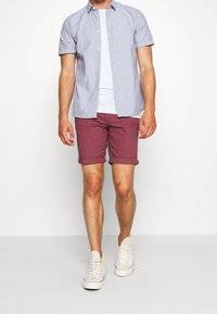 Košile s krátkým rukávem se vzorem v světle modré barvě, zapnutá, s texturovaným povrchem, v kombinaci s těsnými vínovými šortkami a bílými teniskami s vysokým střihом.