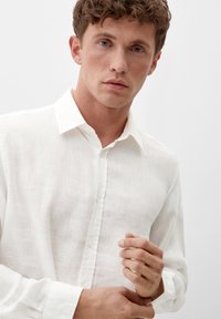 Weißes Leinenhemd mit Kragen und knöpfbarem Einsatz, langärmlig und aus leicht strukturiertem Stoff.
