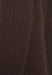 Brunt stickad textil med en mjuk, fluffig yta och vertikala ribbmönster. Materialet ser varmt och tjockt ut, lämpligt för kalla väderförhållanden.
