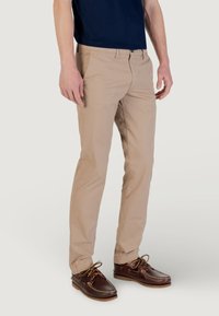 Chinos beige de corte ajustado, fabricados en algodón ligero, con una cinturilla estándar, bolsillos frontales y puños rematados.