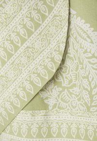 Tessuto verde con un motivo floreale e fogliare bianco, caratterizzato da dettagli e bordi intricati, texture liscia e un elemento di design piegato.