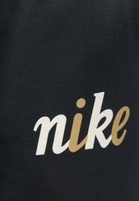 Čierna tkanina s nápisom "nike" v bielom a zlatom písme, so soft textúrou a ležérnym, športovým štýlom.