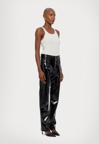 Zwarte hooggerokee, glanzende vinyl broek met een rechte snit, gedragen met een witte tanktop en zwarte puntige hakken. Gladde textuur, minimale details.