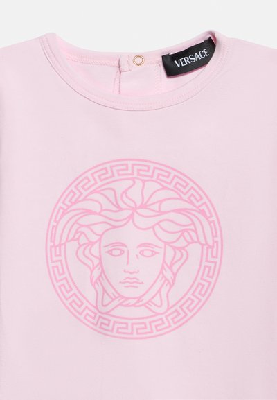 Απαλό ροζ μπλουζάκι με λογότυπο κεφαλής Μέδουσας σε πιο σκούρο ροζ και μαύρη ετικέτα Versace στο πίσω μέρος του λαιμού με κλείσιμο με κουμπί πατιλέτα.