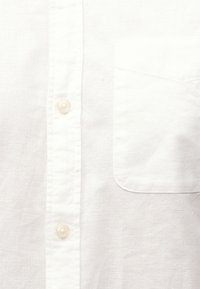 Bela srajca z gumbi iz teksturirane tkanine z žepom na prsih in vrsto svetlih gumbov.
