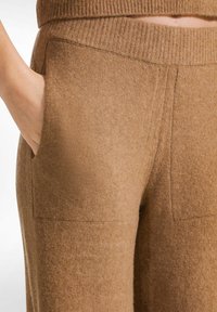 Pantalones de punto en tono marrón con cintura acanalada, bolsillos laterales y una textura suave con detalles de costura sutiles.