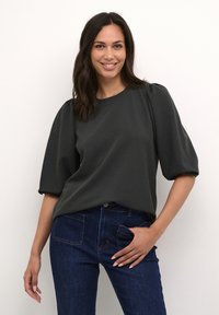 Dark green pullover top with puffed sleeves, round neckline, and textured fabric; paired with dark blue denim jeans featuring back pockets.