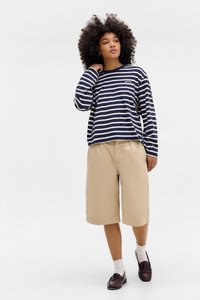 Marineblauwe en witte gestreepte overhemd met lange mouwen en een voorzak, gecombineerd met beige kniebrede shorts en donkere loafers. Witte sokken zichtbaar.