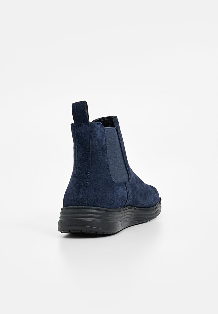 Bottes chevilles en daim bleu marine avec des panneaux latéraux élastiques, une languette et une semelle en caoutchouc noir texturé. Tige lisse, design minimaliste.