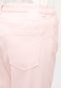 Jeans en denim rose clair vue de dos montrant une poche arrière, des passants de ceinture et des coutures piquées.