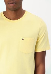 Gul bomulds t-shirt med rund hals og korte ærmer. Har en brystlomme med et lille logo i rød, hvid og blå.