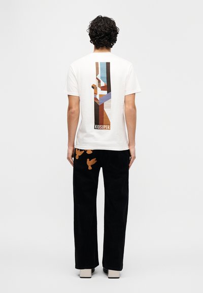 Λευκό κοντομάνικο μπλουζά κι με πολύχρωμο αφηρημένο σχέδιο στην πλάτη· συνδυασμένο με μαύρο παντελόνι που διαθέτει καφέ κέντημα πουλιών.