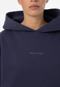 Navy Hoodie aus weichem Stoff, mit einer großen Kapuze und dezentem "PEGADOR"-Logo auf der Vorderseite. Einfaches, lässiges Design.