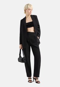 Blazer nero su misura sopra un crop top nero con paillettes, abbinato a pantaloni neri larghi e tacchi a strappo neri; porta una piccola borsa nera.