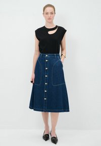 Haut noir à manches courtes avec des découpes, associé à une jupe midi en denim bleu avec des boutons dorés et des poches. Texture lisse, forme évasée.