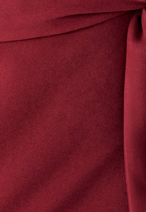 Dieprode stof met een gladde, licht gestructureerde oppervlakte, die plooien en een op maat gemaakte naad of randdetail toont.