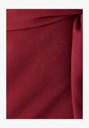 Tissu rouge profond avec une surface lisse et légèrement texturée, présentant des plis et un détail de couture ou de bord soigné.