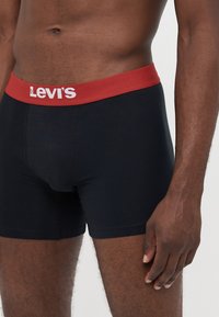 Svarte bomullboxershorts med rød elastisk midje som har "Levi's"-logoen i hvitt. Stoffet har en glatt, stretchy tekstur.