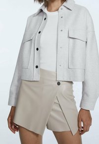 Jasnoszara krótka kurtka z zatrzaskami, dwoma przednimi kieszeniami i miękką fakturą, zestawiona z beżową spódnicą typu wrap z imitacji skóry.