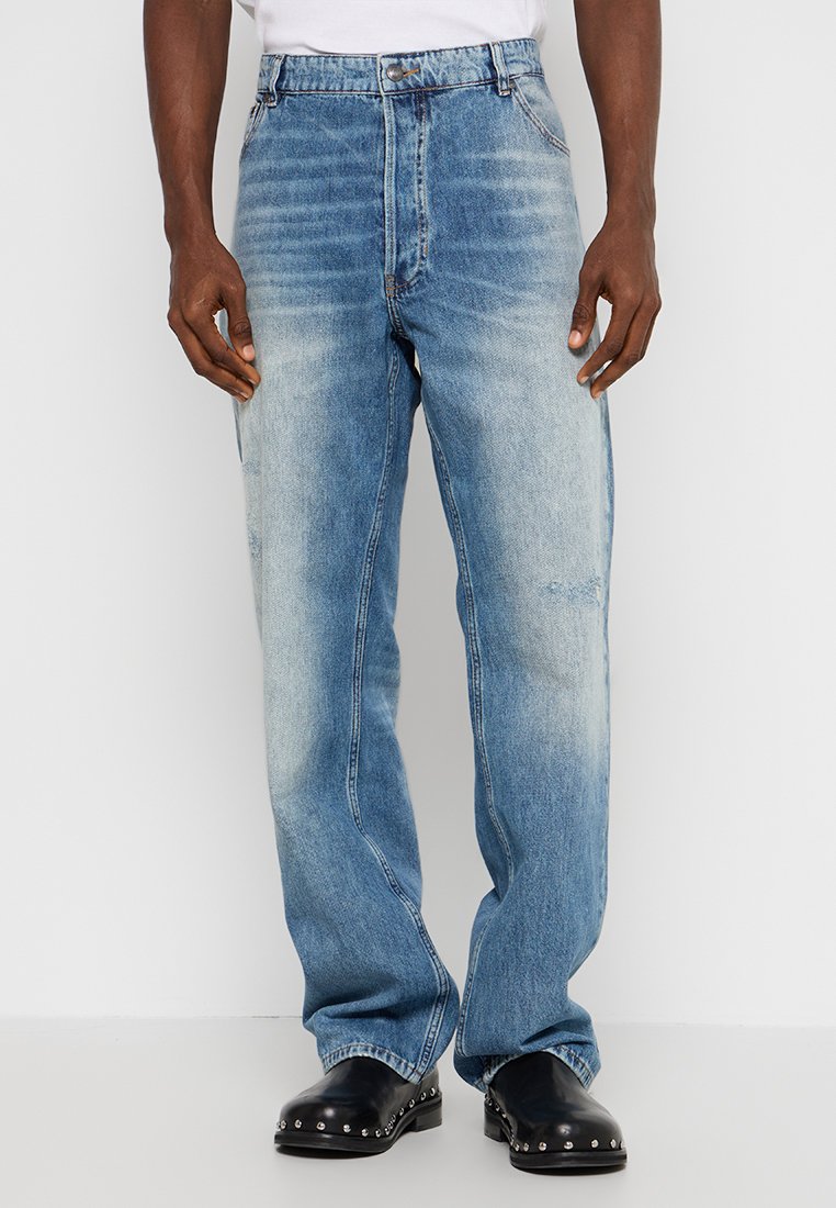 Jean en denim bleu clair avec une coupe décontractée, texture délavée et détails de couture visibles. Présente des poches standard et une fermeture à bouton.