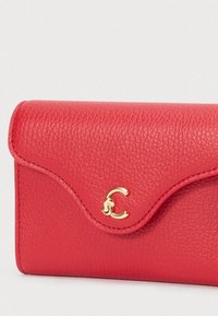 Červená texturovaná kožená peněženka s oblým klopou a malým zlatým dekoračním uzávěrem na bílém pozadí.