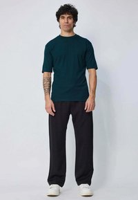 T-shirt à manches courtes bleu canard, associé à un pantalon noir ample. Le tissu semble lisse et l'ensemble présente une coupe décontractée.