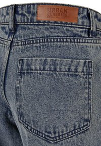 Denim jeans in light blue with a distressed texture. Features a leather patch labeled "URBAN CLASSICS" and a single back pocket.