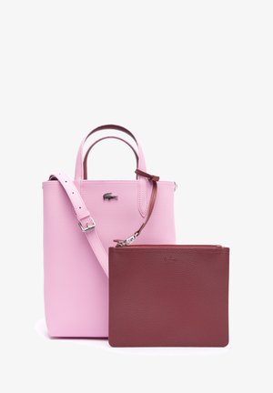 Bolso de cuero rosa con asas superiores y correa ajustable, mostrado con un estuche de cuero marrón con cremallera desmontable en la parte delantera.