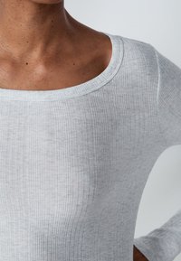Top grigio chiaro a maniche lunghe con costine, caratterizzato da un ampio scollo. Il materiale appare morbido e leggermente trasparente con una sottile texture.