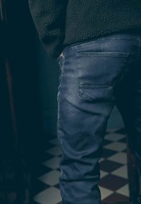 Jeans en denim bleu foncé avec un design classique à cinq poches, légères décolorations et détails de couture, portés avec un haut en matière polaire noire.