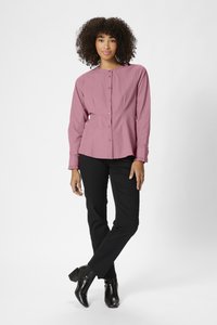 Chemise à manches longues, à boutons, en doux tissu mauve avec un col arrondi et des poignets froncés, associée à un pantalon noir ajusté et des bottines.